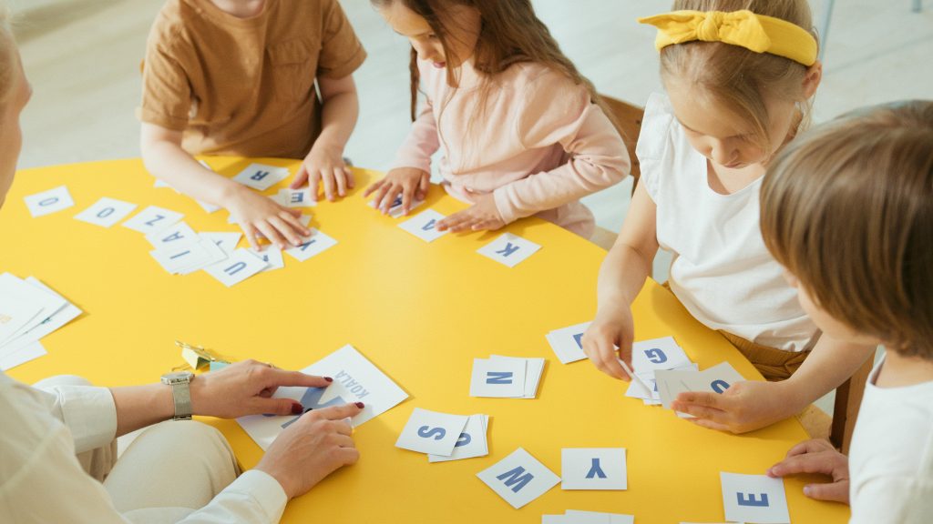 Group of children engaging with alphabet cards on a bright yellow table for learning.